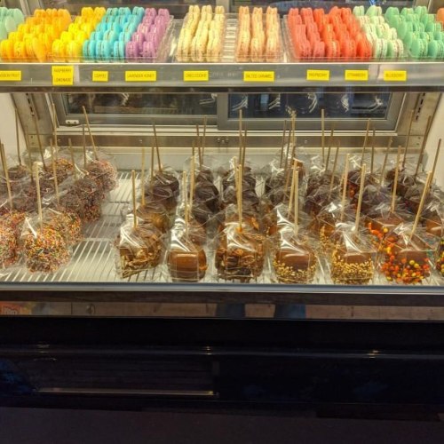 A display case filled with colorful macarons and caramel apples topped with various sprinkles and nuts.
