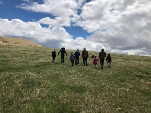 A group of people walking together across a grassy field under a cloudy sky.
