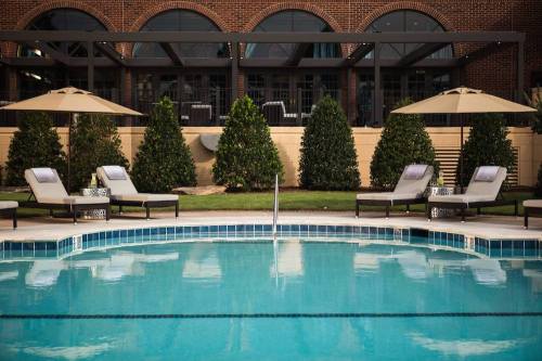 A serene pool area with lounge chairs and umbrellas, surrounded by neatly trimmed hedges and a brick building in the background.