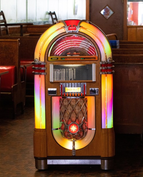 A vintage jukebox with colorful lights, set in a retro diner with wooden booths and red seating.