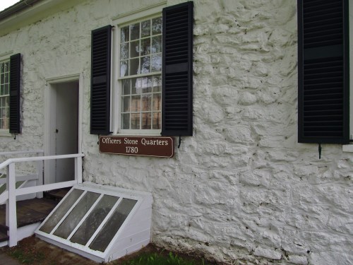 Historic stone building with a sign reading "Officers Stone Quarters 1780" and green shutters on the windows.