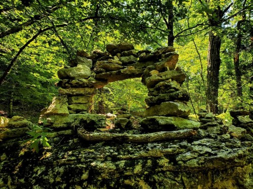 A stone archway surrounded by lush green trees and foliage in a forested area.