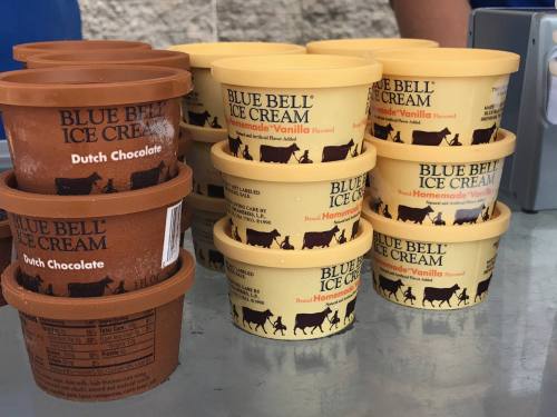 Two stacks of Blue Bell ice cream tubs in Dutch Chocolate and Homemade Vanilla flavors on a table.