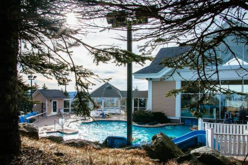 A scenic view of a pool area with water slides, surrounded by trees and a building, under a bright sky.