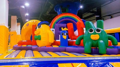 Colorful inflatable play structure featuring cartoon animals and a rainbow, set in a fun indoor environment.