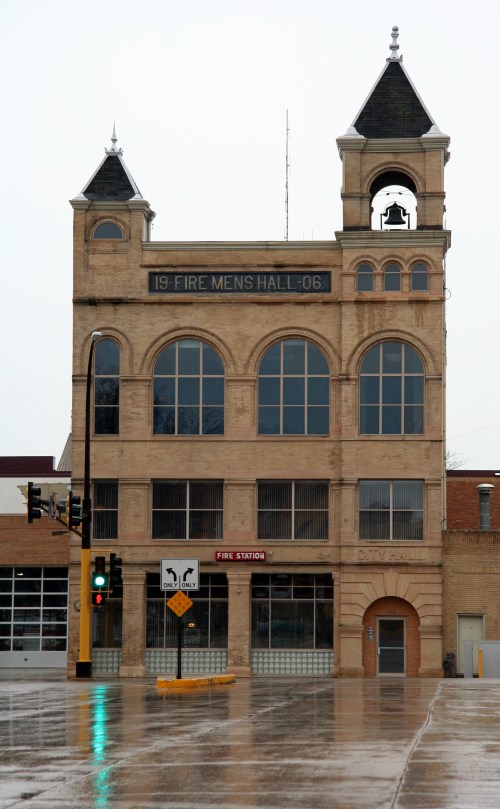Historic fire station building with a bell tower, featuring large windows and a sign reading "Fire Men's Hall 1906."