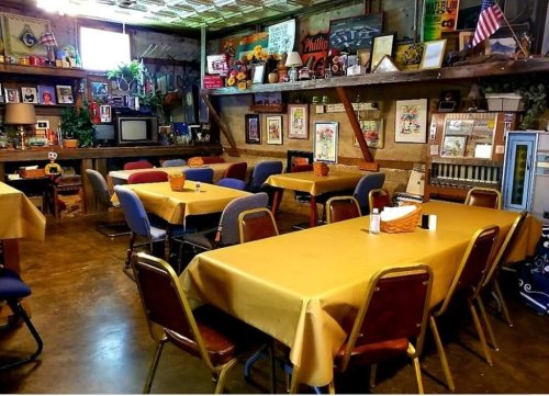 Cozy dining area with yellow tablecloths, wooden decor, and vintage items on shelves in a rustic setting.