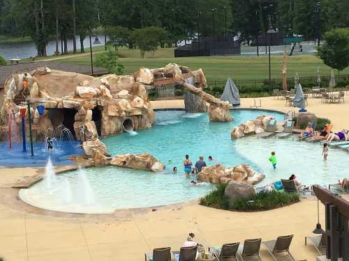 A family-friendly pool area with a rock slide, water features, and children playing in the water on a sunny day.