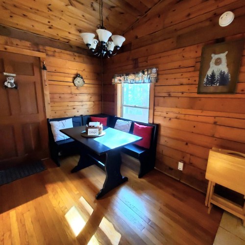 Cozy wooden dining area with a black table, cushioned bench seating, and a chandelier, illuminated by natural light.