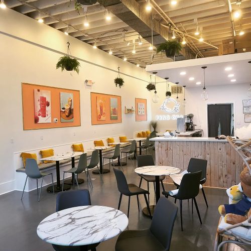 Bright café interior with marble tables, black chairs, colorful wall art, and hanging plants. Cozy and inviting atmosphere.