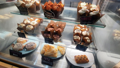 Display case filled with various cupcakes and pastries, including cinnamon rolls, apple turnovers, and spinach pastries.