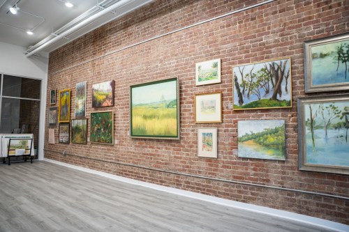 Art gallery interior featuring various framed paintings on a brick wall with wooden flooring.
