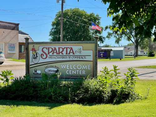 Sign for the Sparta Area Chamber of Commerce Welcome Center, featuring greenery and an American flag in the background.