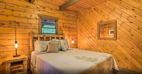 Cozy cabin bedroom with wooden walls, a bed with decorative pillows, and warm lighting.