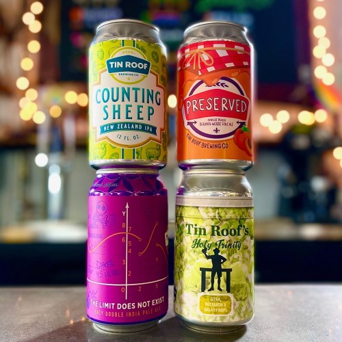 Four colorful beer cans stacked on a table, featuring designs for Tin Roof Brewing Co. and various beer names.