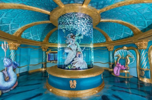 A vibrant underwater-themed room featuring a central fish tank, ornate decorations, and colorful marine life.
