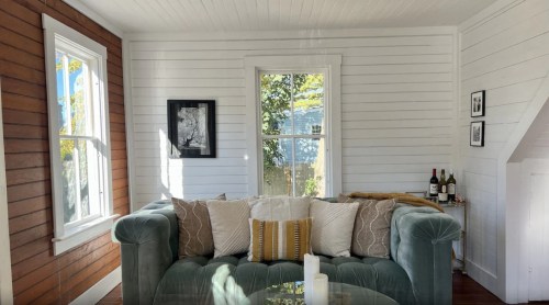 Cozy living room with a green sofa, decorative pillows, a glass table, and sunlight streaming through a window.