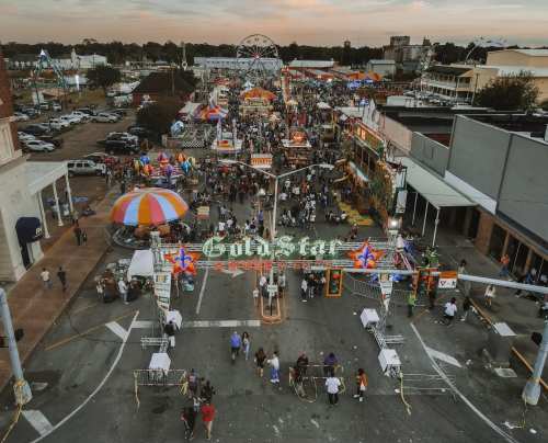 Aerial view of a bustling carnival with colorful tents, rides, and crowds enjoying the festivities at sunset.