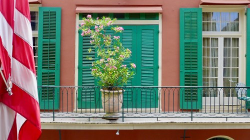 A vibrant green shuttered window with a potted plant on a balcony, framed by a red and white striped flag.