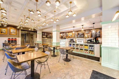 A modern café interior with tables, a service counter, and decorative lighting. A staff member is at the counter.