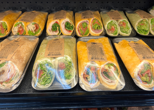 A display of various wrapped sandwiches with colorful fillings, neatly arranged in a refrigerated case.