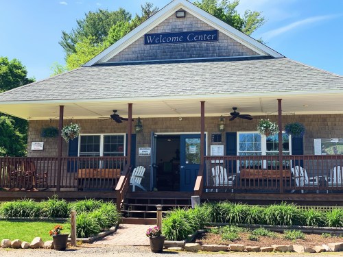 A welcoming center with a porch, rocking chairs, and flower pots, surrounded by greenery and blue skies.
