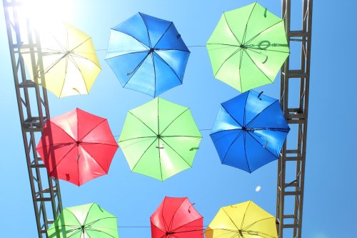 Colorful umbrellas in yellow, green, blue, and red suspended against a bright blue sky.