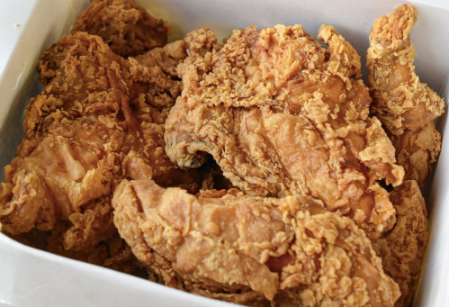 A close-up of crispy, golden-brown fried chicken pieces in a white takeout box.