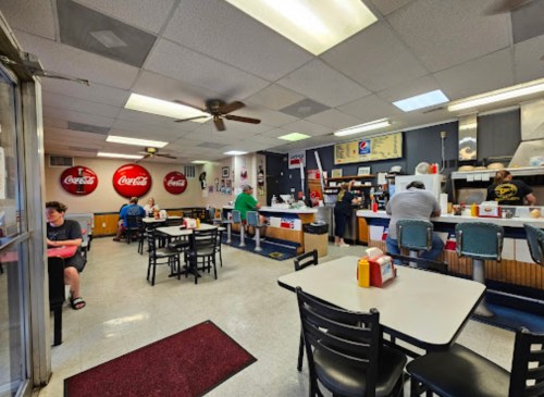 A casual diner interior with patrons at tables and a counter, featuring Coca-Cola and Pepsi branding on the walls.