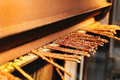 Close-up of crispy, golden-brown sticks resting on a metal surface, likely from a cooking or baking process.