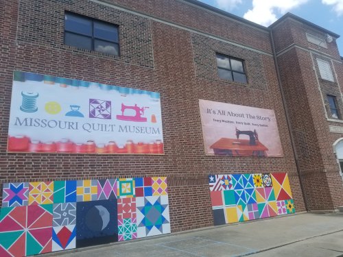 Exterior of the Missouri Quilt Museum featuring colorful murals and banners about quilting and storytelling.