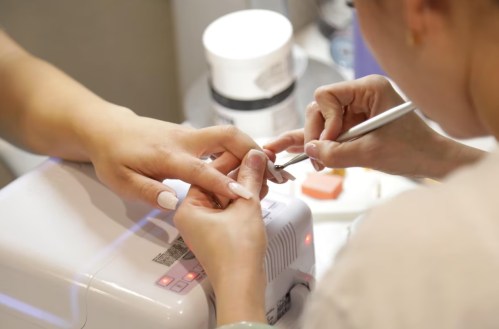 A close-up of a nail technician applying nail polish to a client's fingers at a salon.