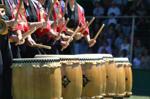 A group of drummers in colorful outfits playing large wooden drums outdoors.