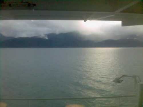 A view from a ship showing calm waters and distant mountains under a cloudy sky.