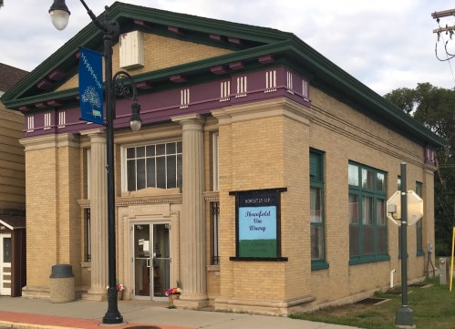 A historic brick building with columns, featuring a sign for "Brookfield Vine Winery" and decorative purple trim.