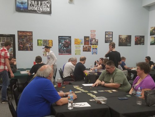 A game store with people playing tabletop games at various tables, surrounded by posters and a relaxed atmosphere.