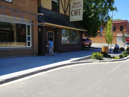 A person enters a café with a sign reading "Main Street Café" on a sunny day, with a sidewalk and street visible.