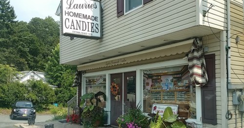 Exterior of Laurie's Homemade Candies shop, featuring a sign, window displays, and a parked car nearby.