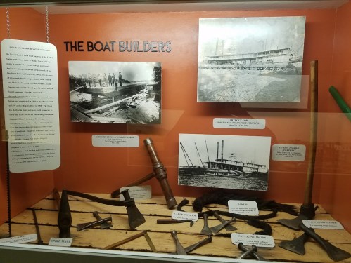Display of historical boat-building tools and photographs, showcasing the craftsmanship and techniques used in boat construction.
