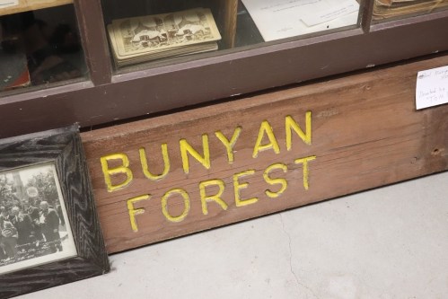 A wooden sign reading "BUNYAN FOREST" in yellow letters, displayed in a glass case with historical items.