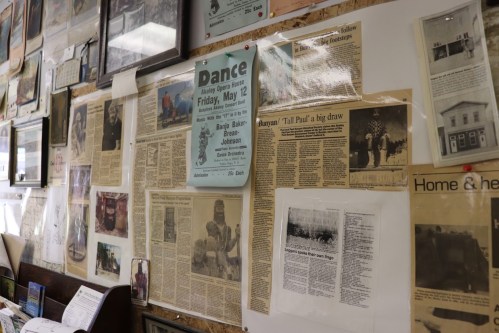 A wall covered with various newspaper clippings, photos, and a dance event poster.