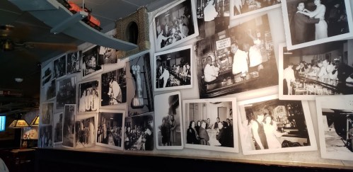 A wall covered with black-and-white historical photographs depicting people in a bar setting.