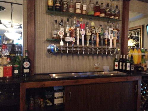 A bar with various liquor bottles, beer taps, and a cocktail glass on the counter.