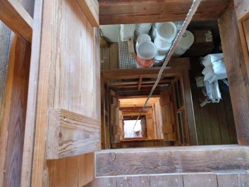 View looking down a wooden staircase with a rope, revealing multiple levels and storage items below.