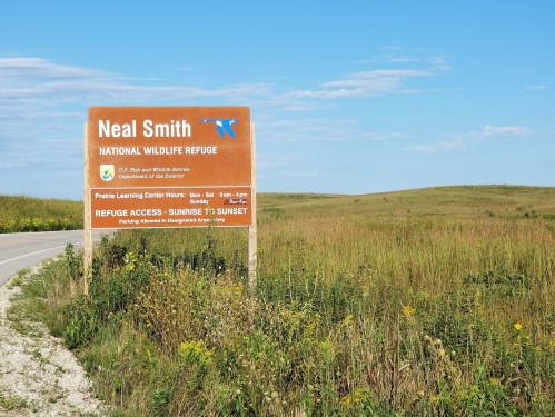 Sign for Neal Smith National Wildlife Refuge, with grassy fields and a clear blue sky in the background.