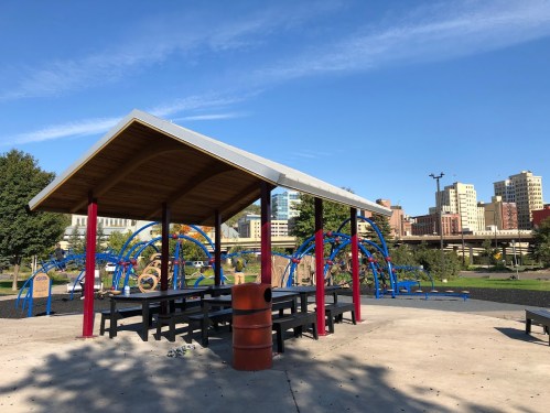 A playground with colorful equipment and a shaded picnic area under a clear blue sky.