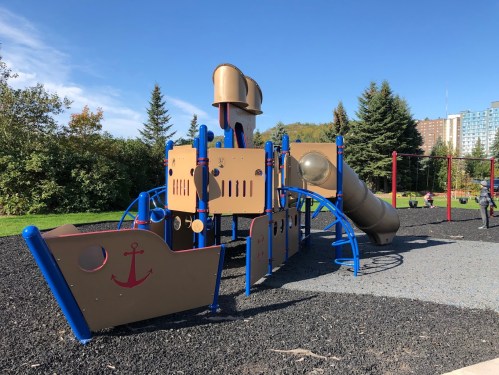 A colorful playground structure designed like a pirate ship, featuring slides and climbing areas, set in a park.