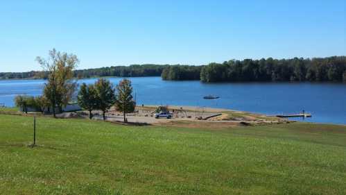 A serene lake view with green grass, trees, and a small dock, under a clear blue sky.