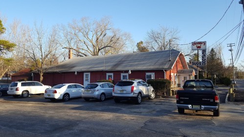 A red seafood restaurant with parked cars outside, surrounded by trees and a clear blue sky.