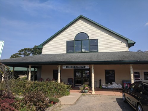 A two-story building with a sign reading "Sheep Shoppe," surrounded by greenery and a clear blue sky.